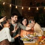Group of friends taking a selfie at a dinner table, with plates and drinks in front of them in a cozy restaurant setting.